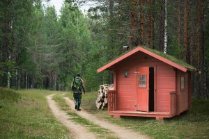 man in hunting gear next to small red cabin