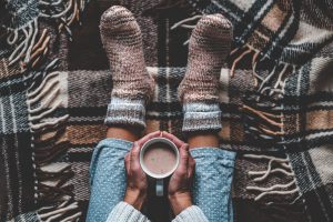 feet of woman in knitted socks sitting holding mug of cocoa