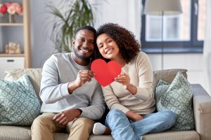 couple sitting on couch holding paper heart